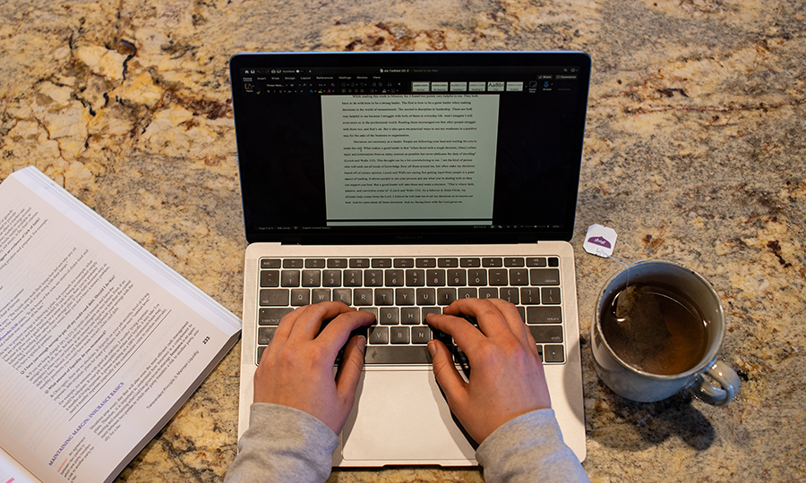 Student typing on their computer with coffee