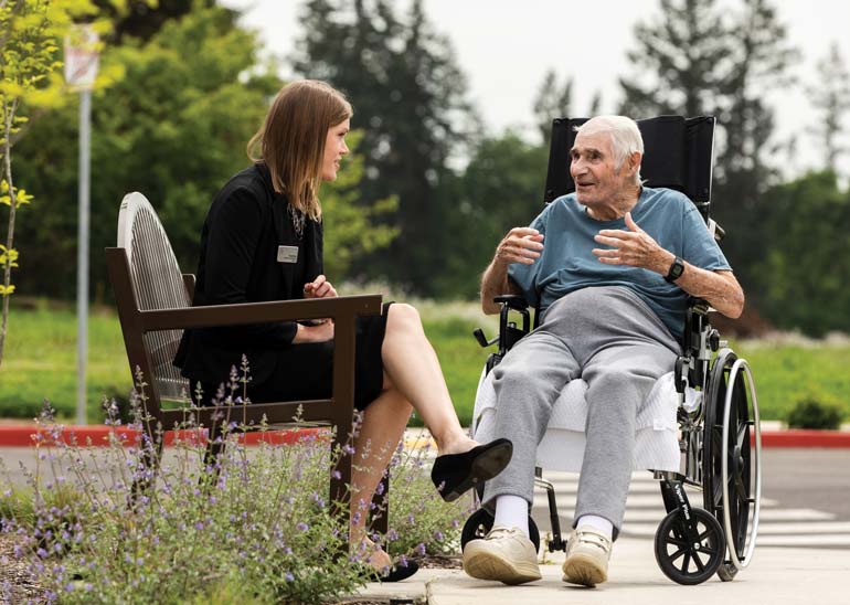 Tracy Berg sitting outside talking with an elderly man in a wheelchair