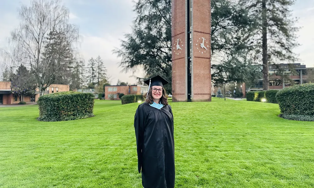 Sara Noelle Goodman in graduation robe standing on the campus quad