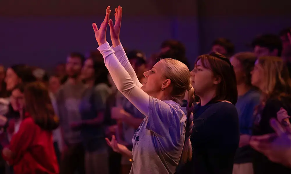 A student lifts her hands in worship in a pink glow