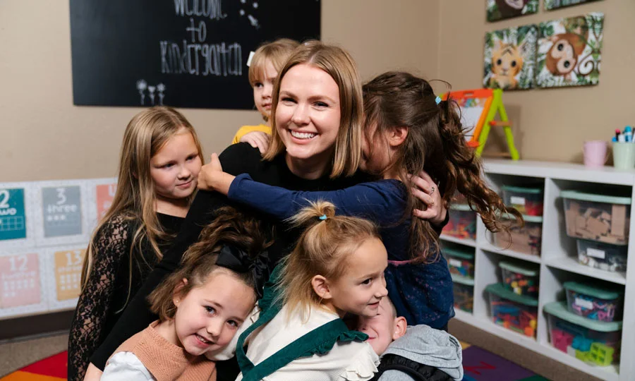 Teacher smiles and hugs her class