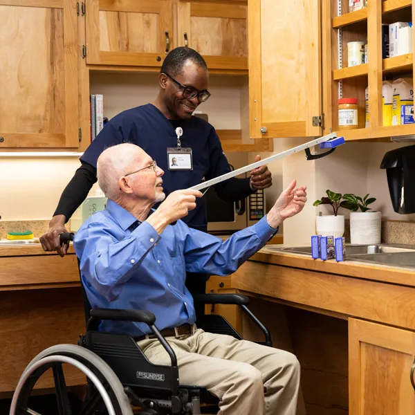 An OT student helps and elder reach something in the kitchen